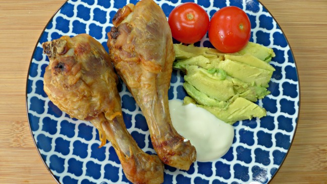 A plate of low carb high fat foods - chicken legs, avocado, tomato and sour cream