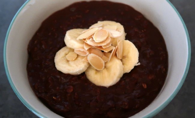 Bowl of chocolate and banana oatmeal topped with sliced bananas and roasted almonds