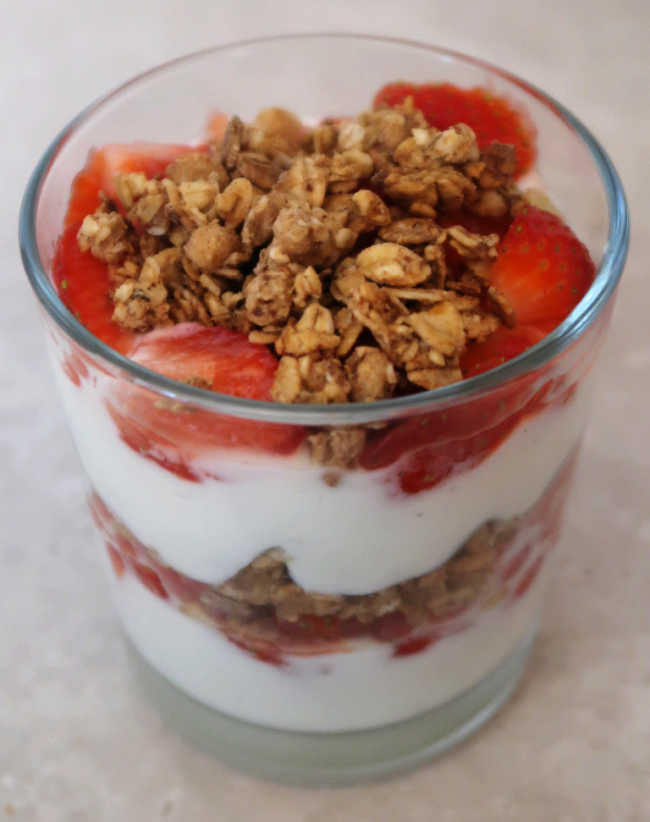 Glass with layered strawberries granola and yogurt in a parfait dessert